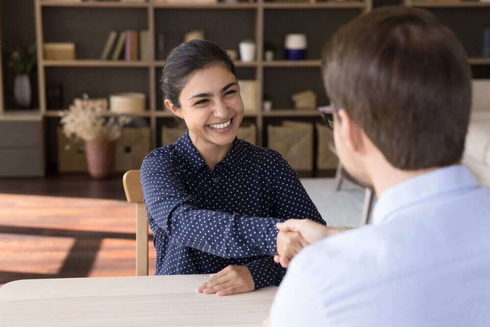 Woman shaking hand of person interviewing her for role at company.